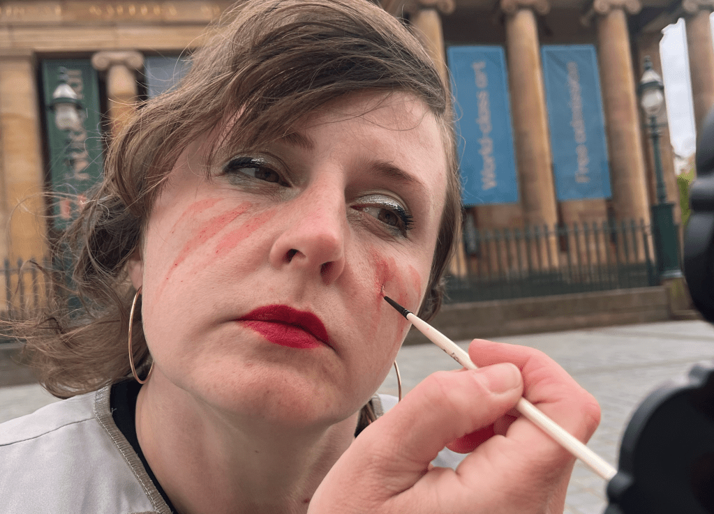 A person painting on her own face with pale orange pigment